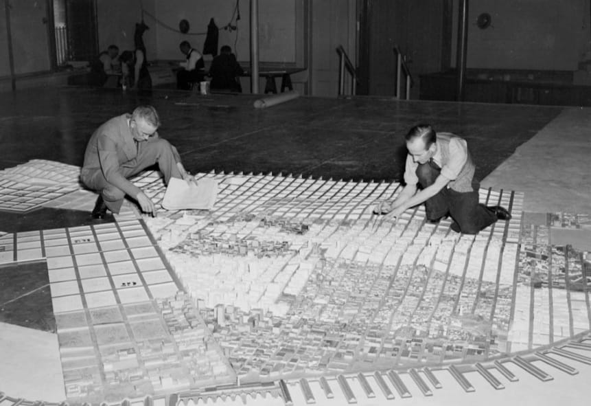 Two men work on a scale mode of San Francisco in a large room.