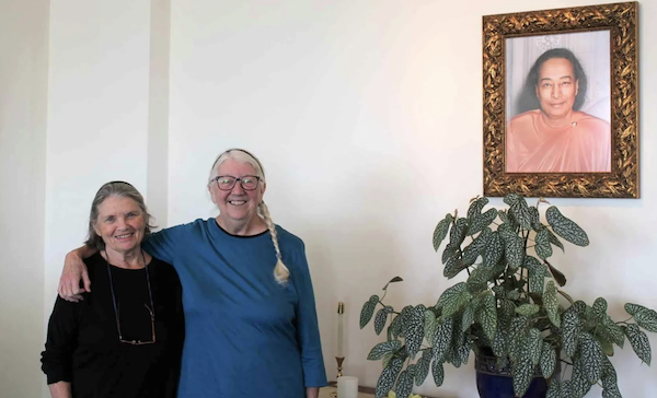 Two women stand before a painting of their spiritual leader.