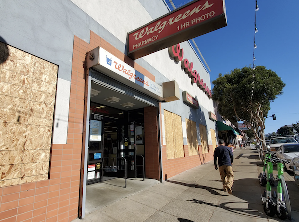 People walk past a storefront with broken windows.