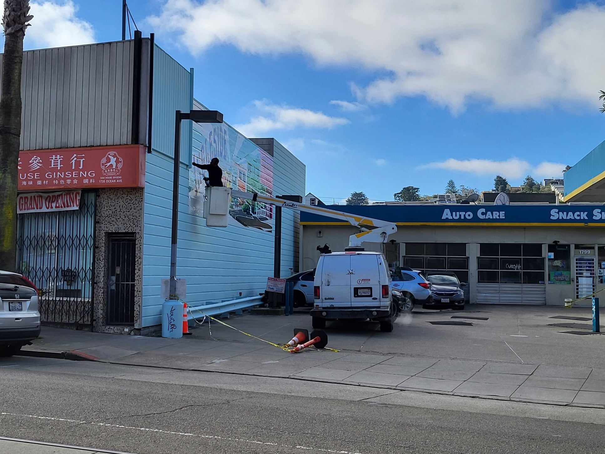 Man in bucket ladder places mural on wall.