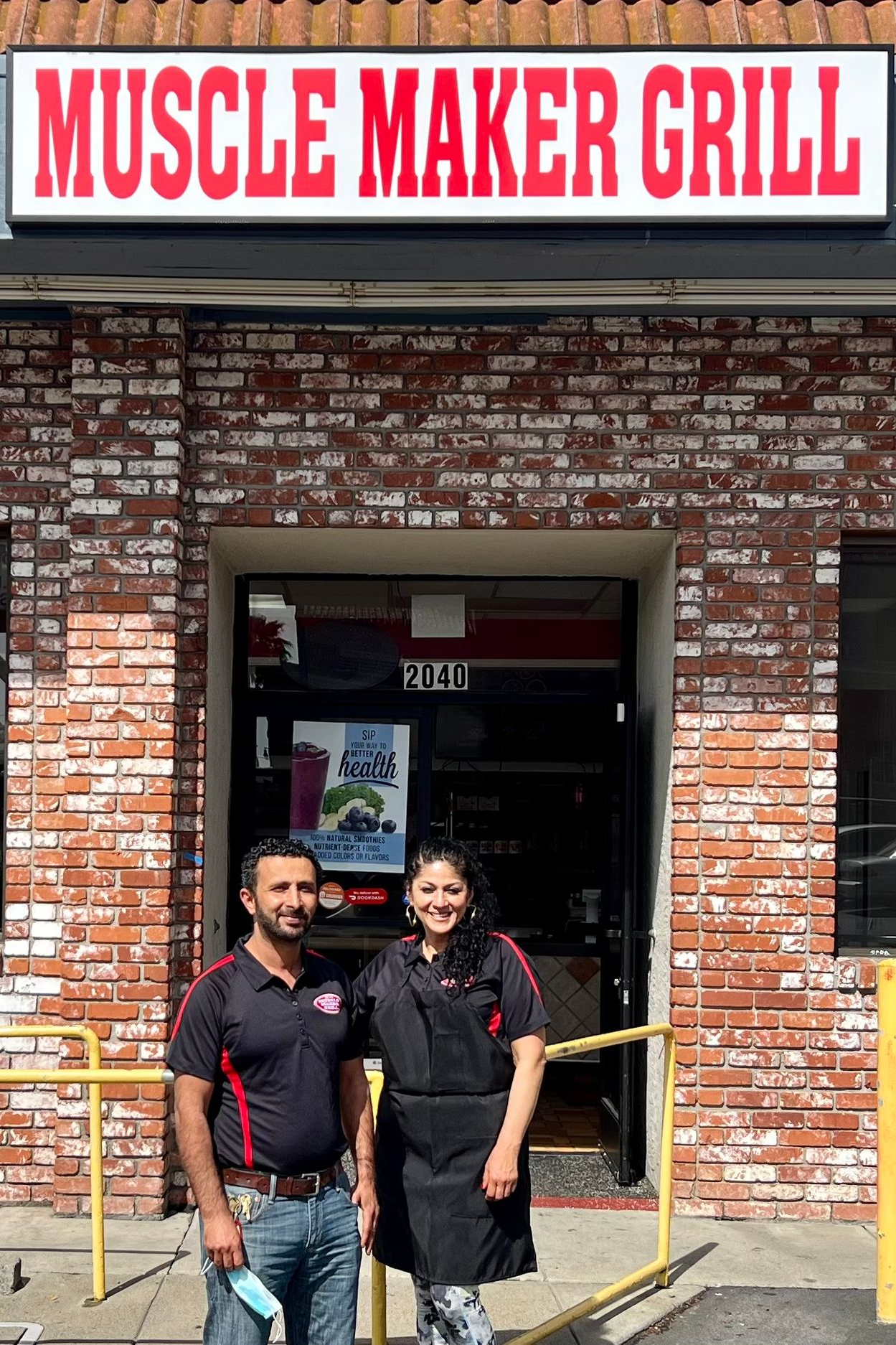 Man and woman pose for photograph in front of small business.
