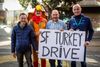 Four people — including one dressed as a turkey — stand with a sign reading SF Turkey Drive.