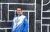 A man stands in front of a mural wearing a blue jacket.