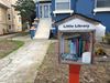 A Little Free Library full of books stands in front of a house.
