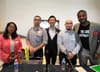 Five people stand behind a table with microphones.