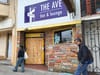 People walk by a boarded up storefront.