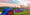 seven tents lined in a diagonal on grass with trees and mountains in the background.